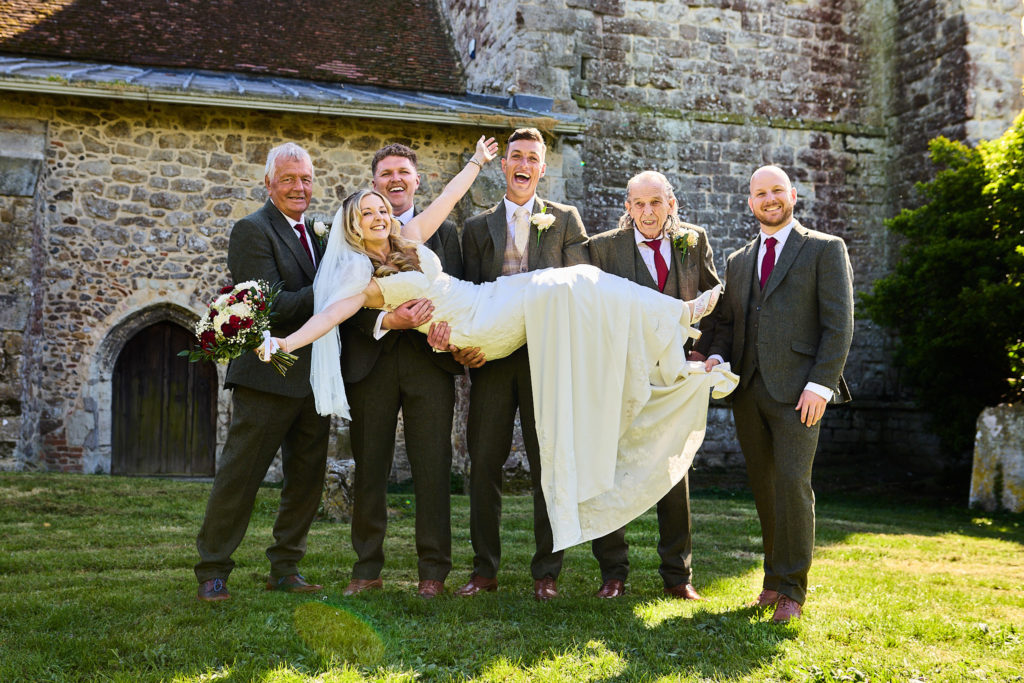 Groomsmen holding the bride up horizontally outside the church