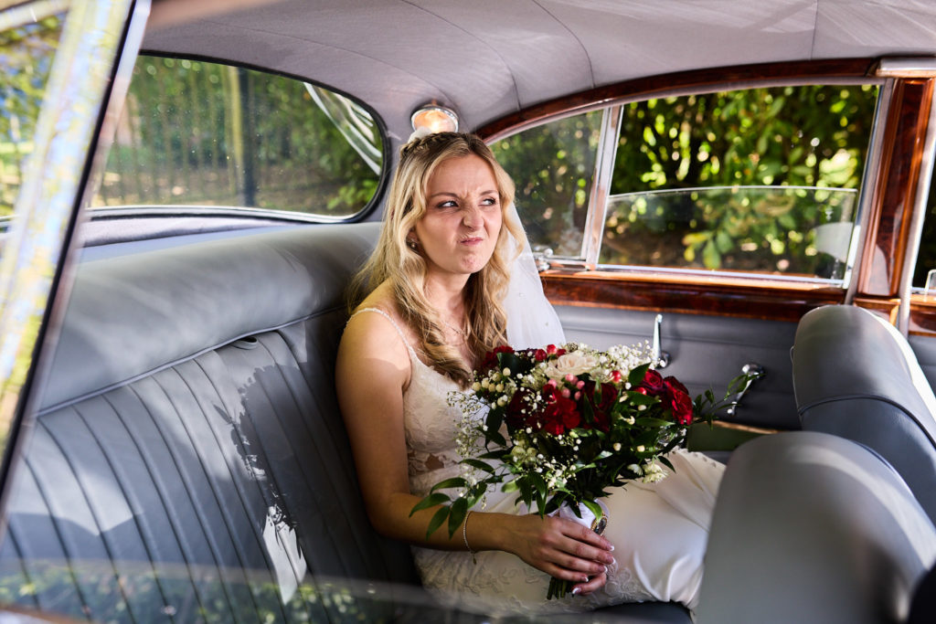 Bride smiling with her bouquet in the back seat of the classic wedding car