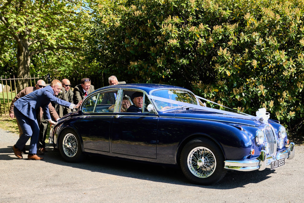 Wedding guests pushing the classic blue Jaguar wedding car