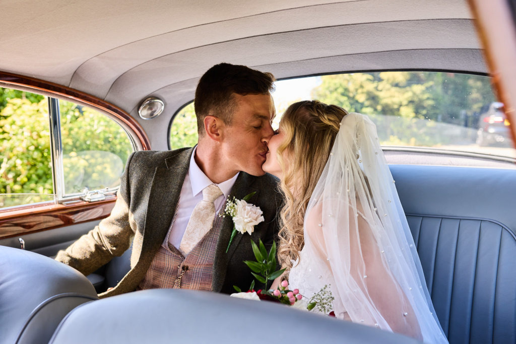 Bride and groom kissing in the back seat of the wedding car