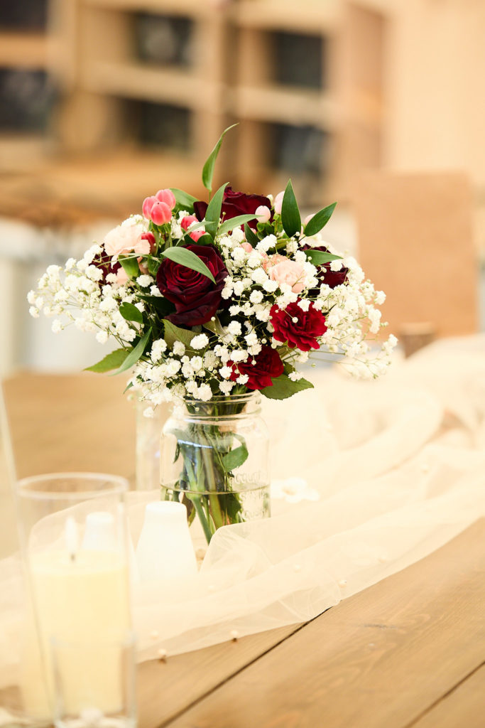 Jar of red roses and gypsophila on a wooden table in the marquee
