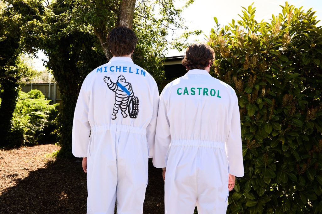 Two men in white Michelin and Castrol racing overalls, seen from behind