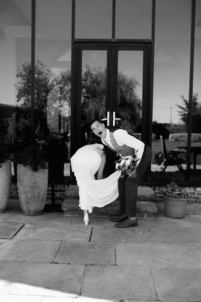 Black and white photo of the groom dipping the bride in front of a black barn