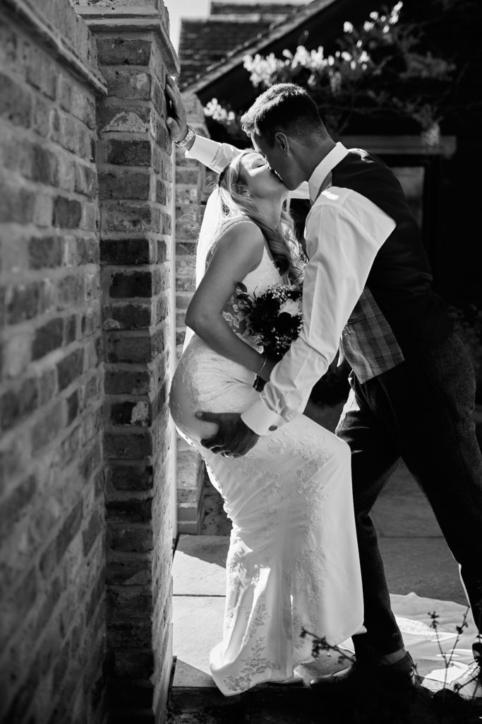 Black and white photo of the bride and groom kissing against a brick wall