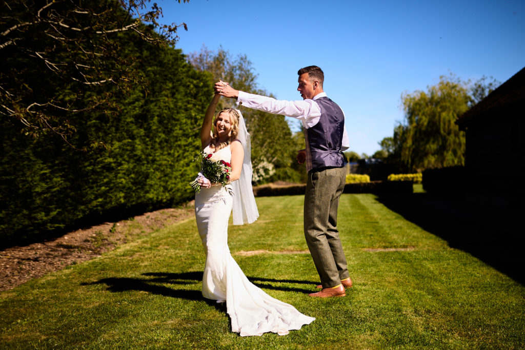 Groom twirling the bride on a lawn under a blue sky