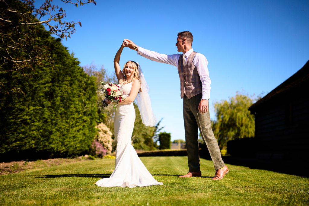 Groom spinning the bride on the lawn beside a tall hedge