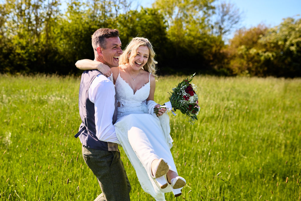 Groom carrying the laughing bride through a meadow