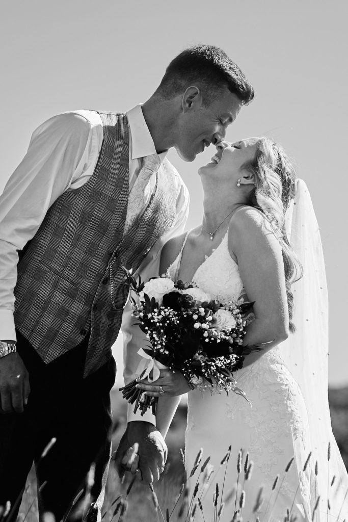 Black and white photo of the bride and groom kissing, seen through long grass