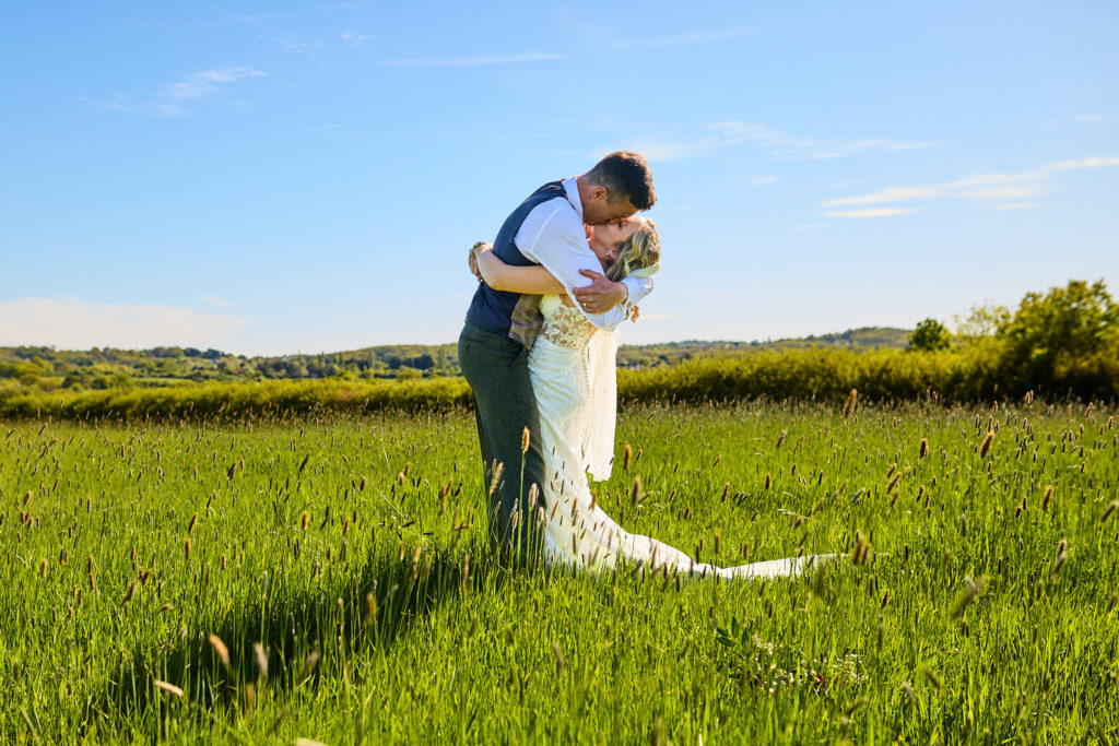Bride and groom hugging in a field under a blue sky