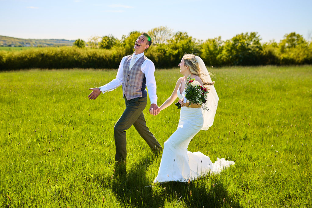 Bride and groom walking hand in hand through a field