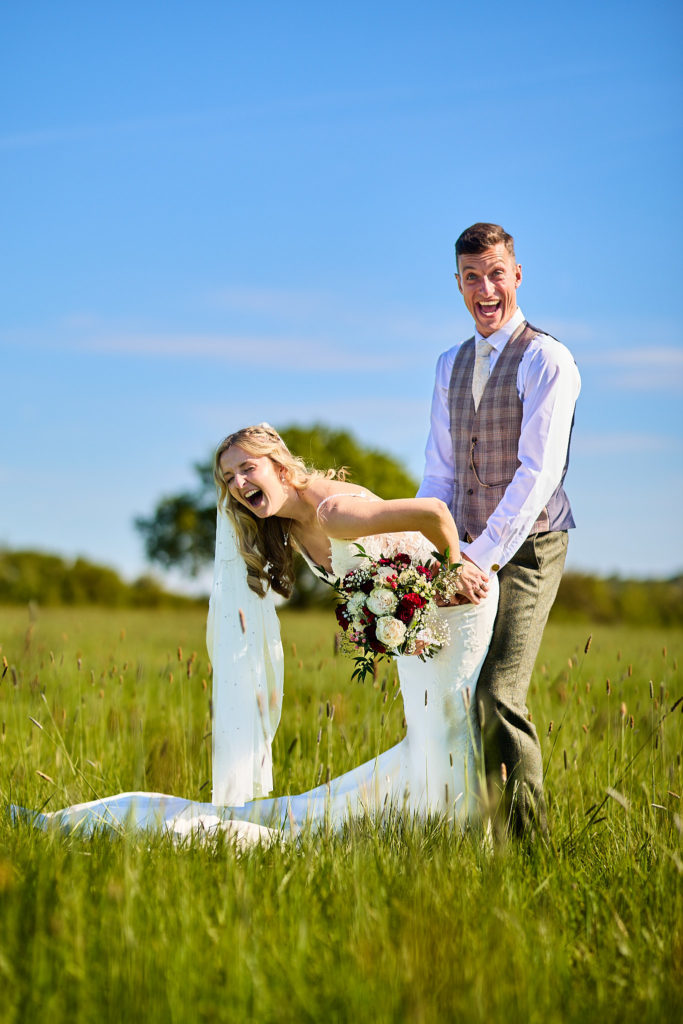 Bride doubled over laughing beside the groom in long grass