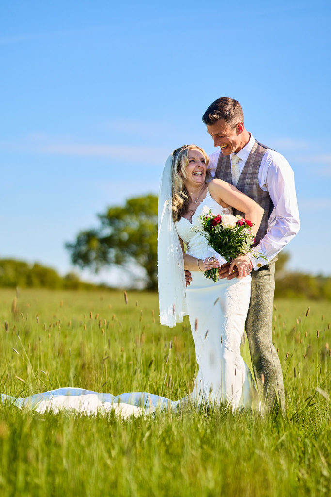 Groom hugging the bride from behind in long grass