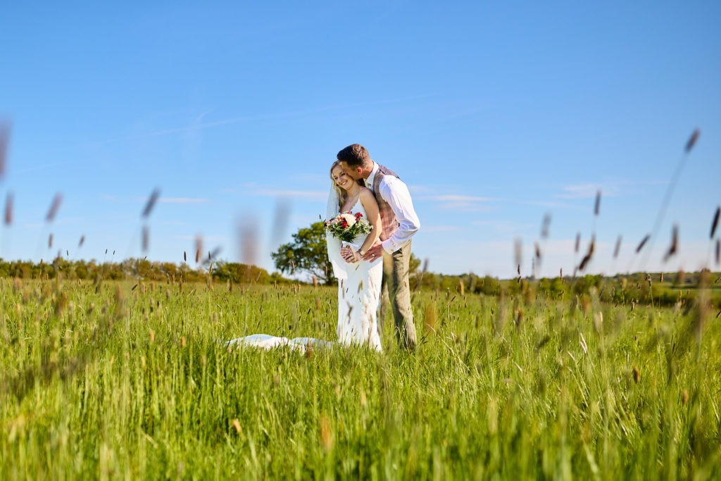 Bride and groom kissing in the distance across a meadow