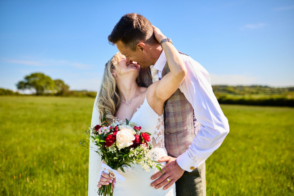 Groom kissing the bride as she wraps her arms round his neck