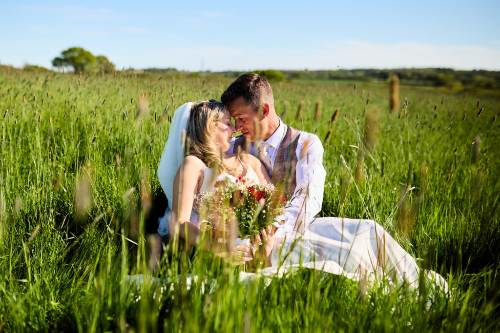 Bride and groom sitting forehead to forehead in long grass