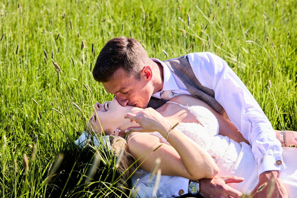 Bride and groom lying in long grass as he kisses her