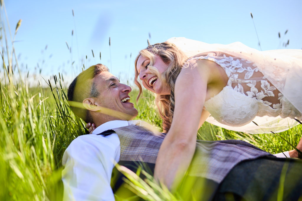 Bride and groom laughing as they lie in long grass