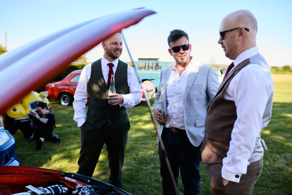 Three men talking beside the open bonnet of a red car at the wedding car show