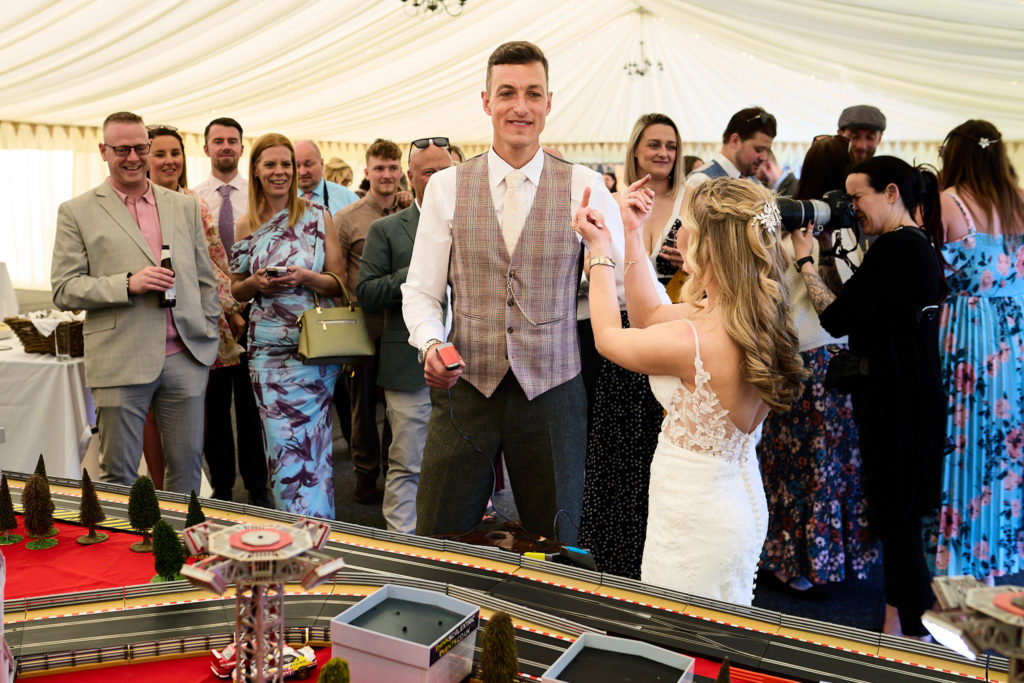 Guests cheering as the bride and groom race Scalextric cars