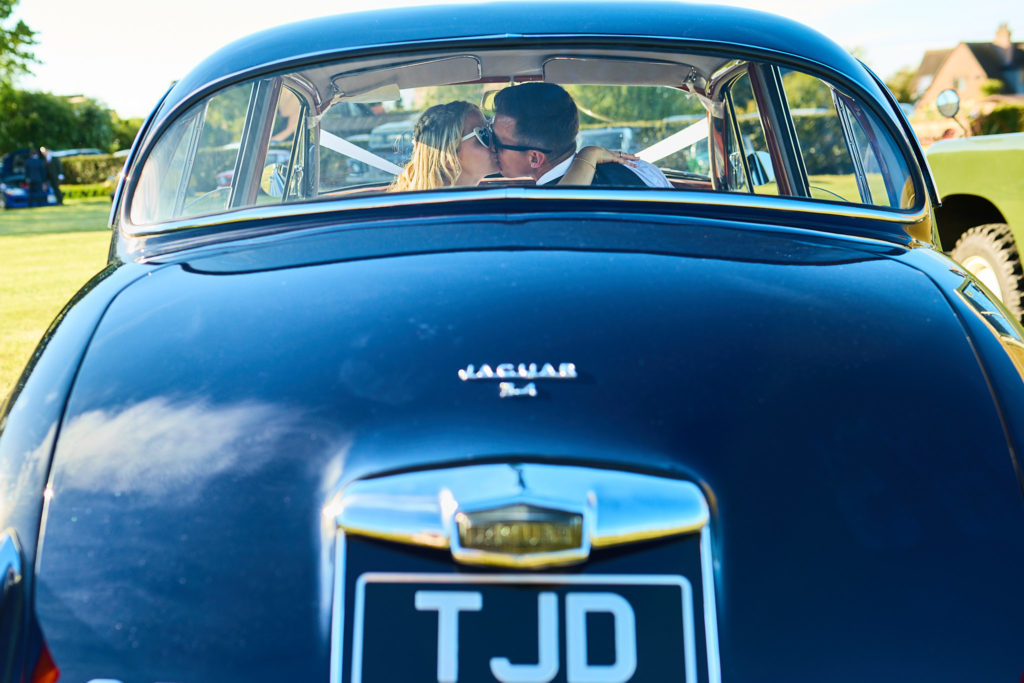 Bride and groom seen through the rear window of a classic blue Jaguar