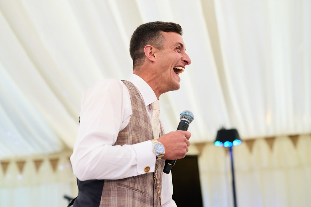 Groom laughing with a microphone during his speech