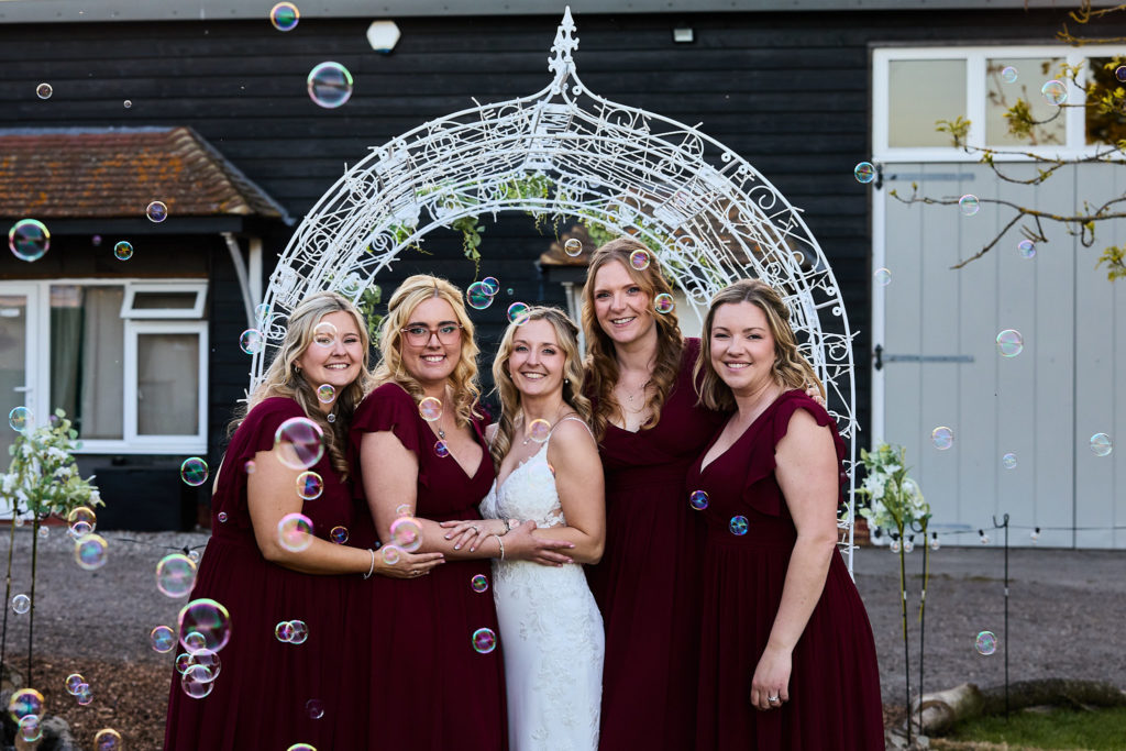 Bride and four bridesmaids in front of an illuminated arch with bubbles in the air