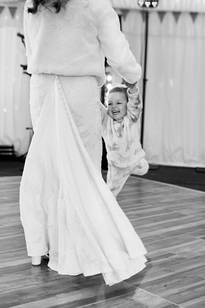 Black and white photo of a toddler running after the bride across the dance floor