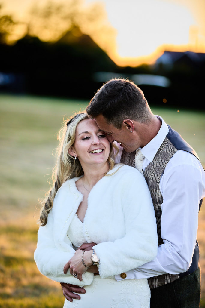 Groom kissing the bride's forehead at golden hour, the bride in a white fluffy jacket