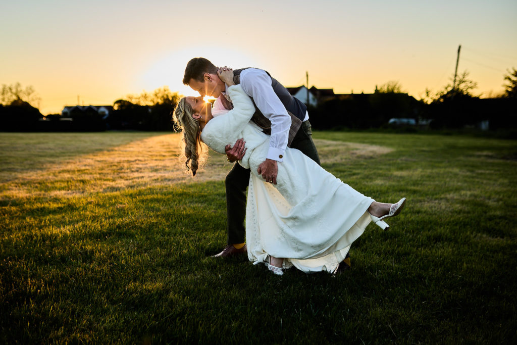 Groom dipping the bride in a field at sunset