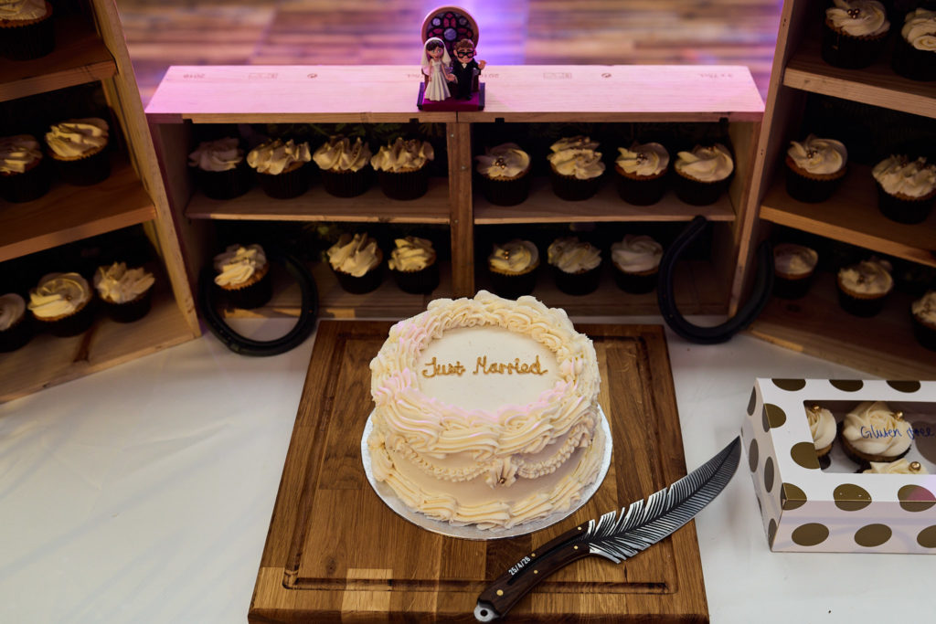 Wedding cake on a wooden board with a knife, in front of a doughnut wall