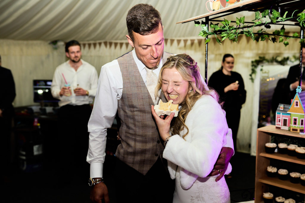 Bride and groom laughing as they eat wedding cake