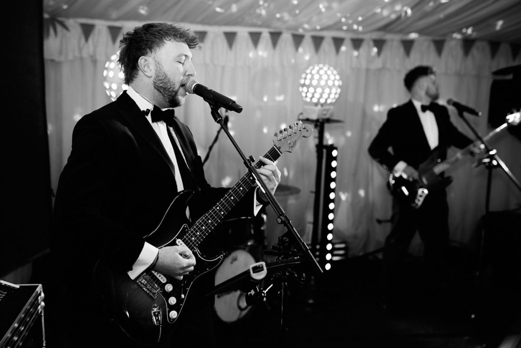Black and white photo of the wedding band's guitarist singing on stage