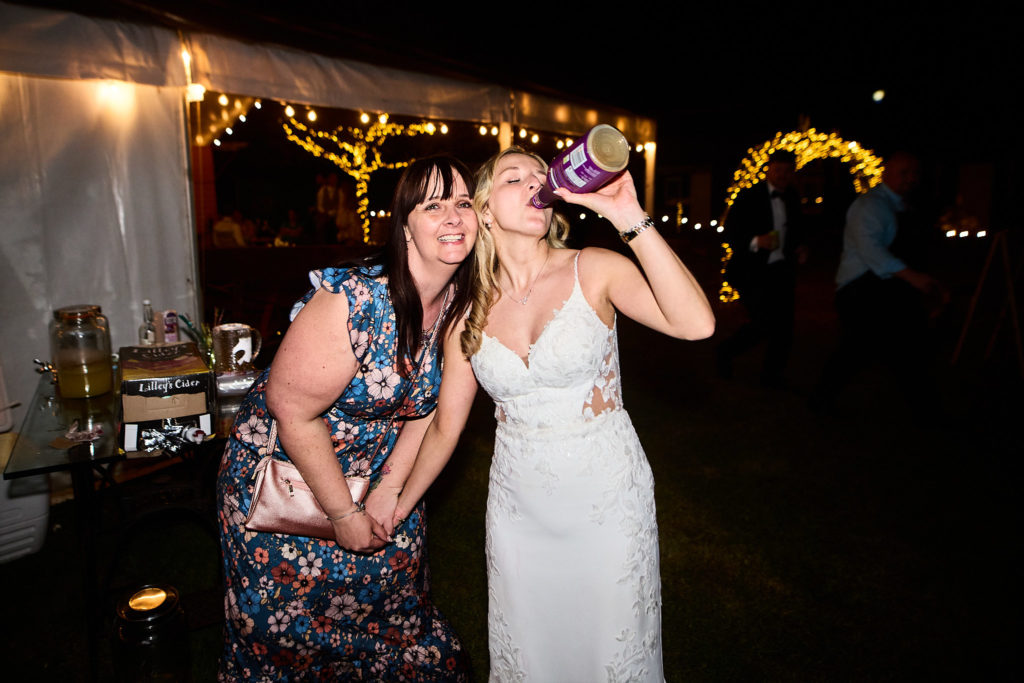 Bride and a guest posing with a drink outside at night