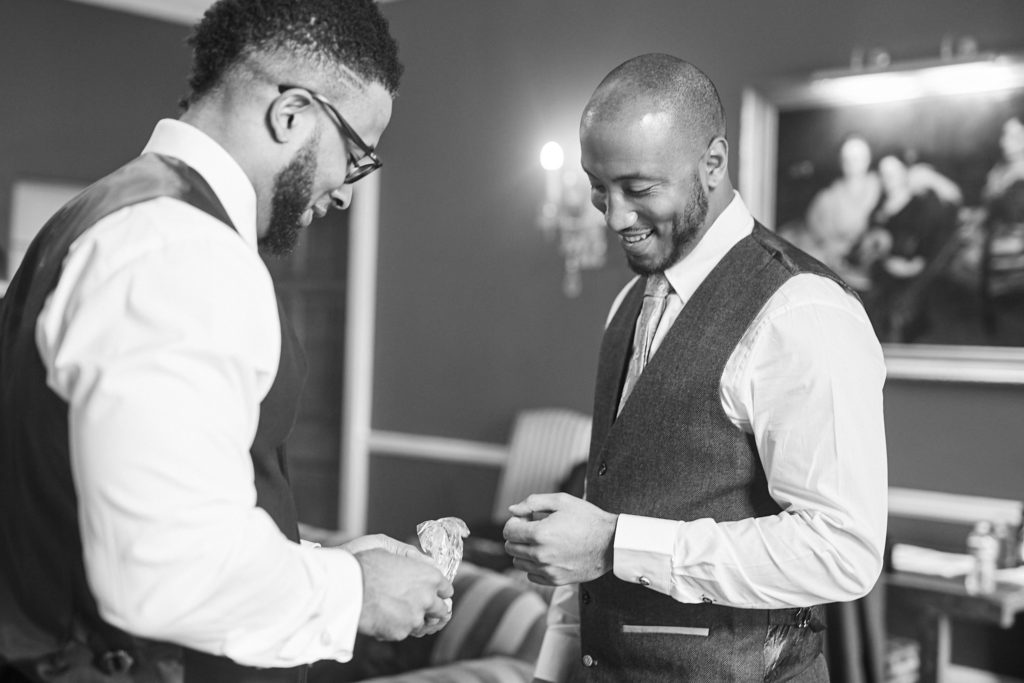 Black and white photo of the groom and a groomsman getting ready in waistcoats