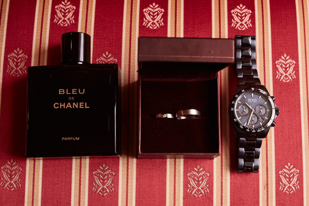 Groom's aftershave, wedding rings and watch laid out on a striped chair