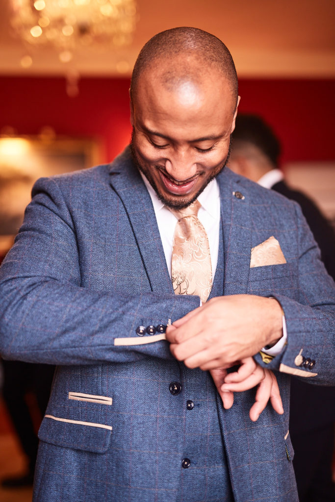 Groom in a blue tweed suit smiling as he fastens his cuff