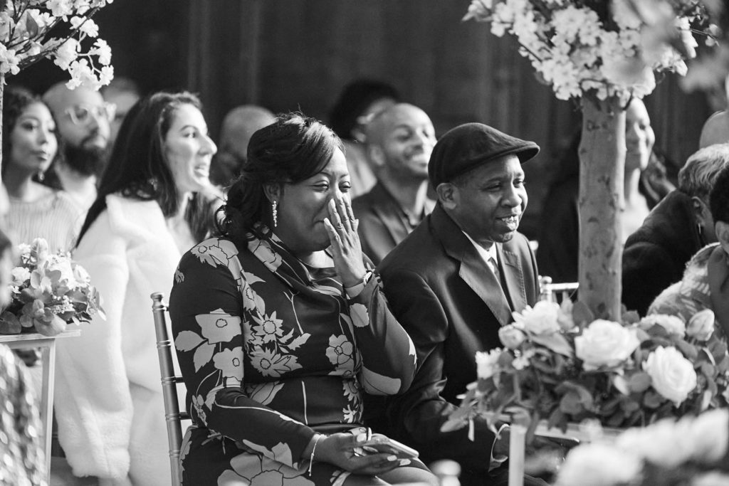 Black and white photo of wedding guests smiling during the ceremony