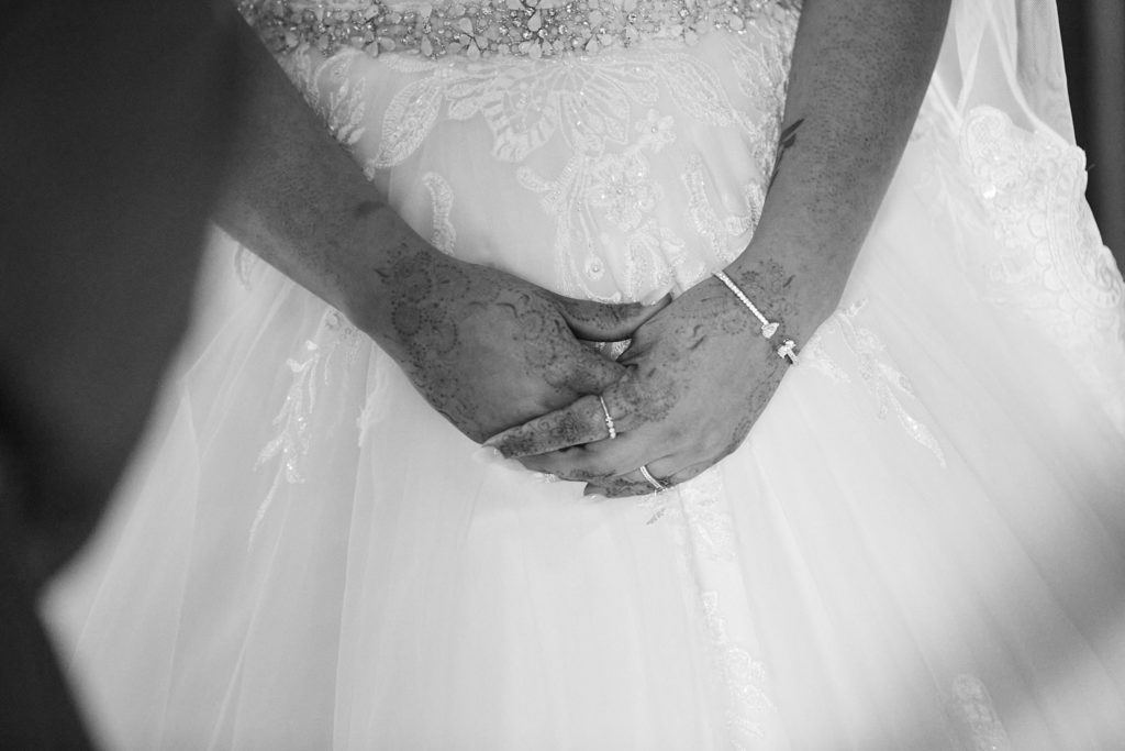 Black and white close-up of the bride's clasped hands against her wedding dress