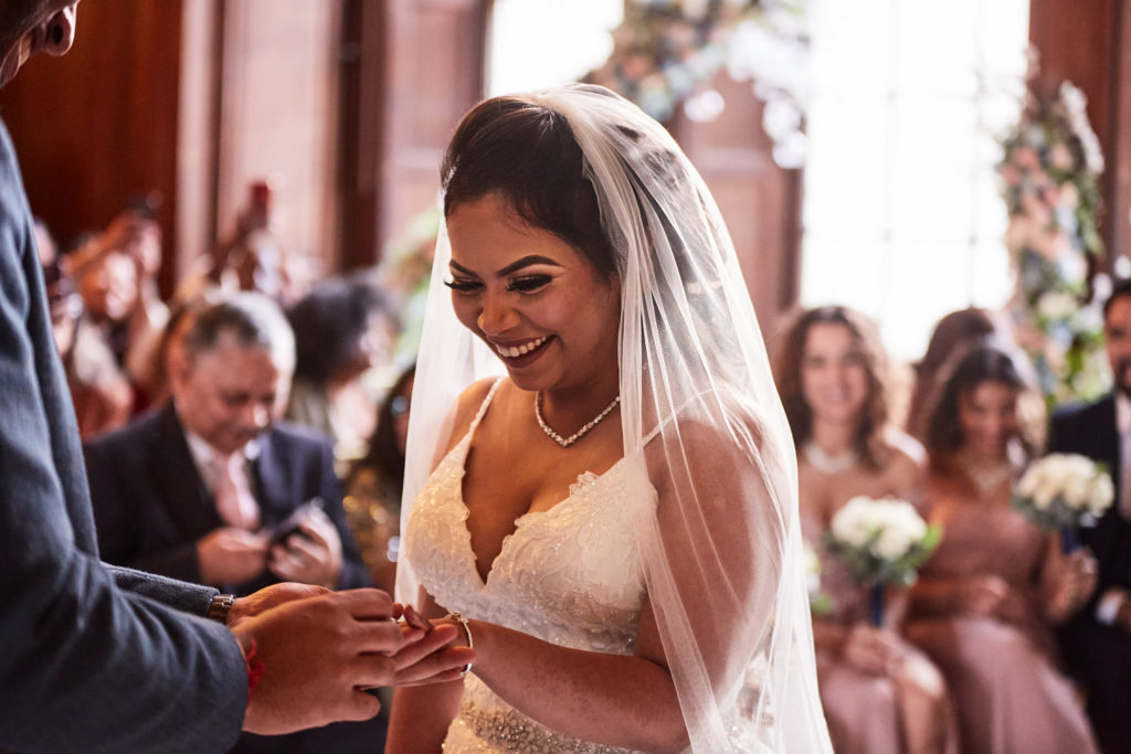 Bride smiling as the groom places the ring on her finger