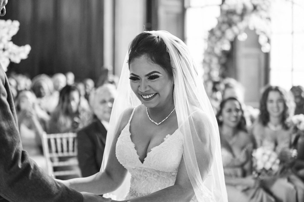 Black and white photo of the bride smiling at the groom during their vows