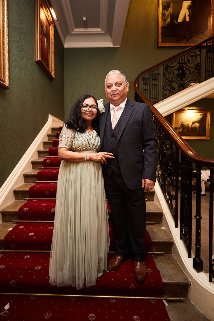 Older couple standing on the red-carpeted staircase at Addington Palace