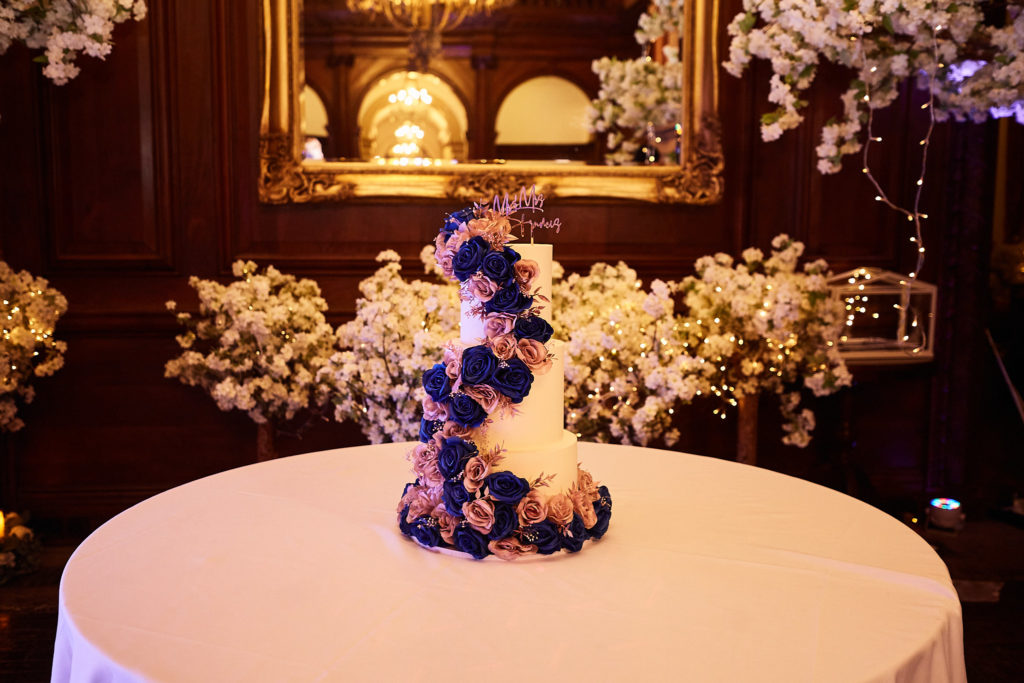 Wedding cake decorated with blue and pink roses in a wood-panelled room