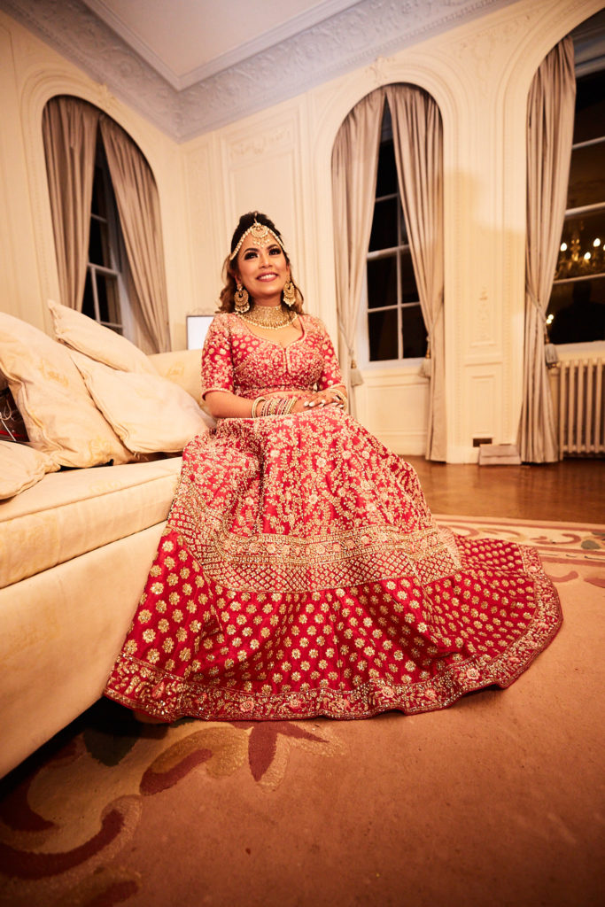 Bride in a red and gold lehenga seated on the floor with her skirt fanned around her