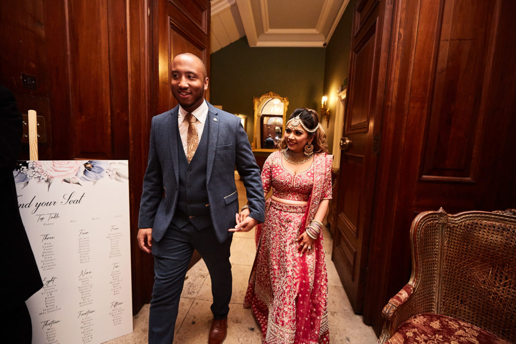 Groom and bride in a pink lehenga arriving beside the table plan