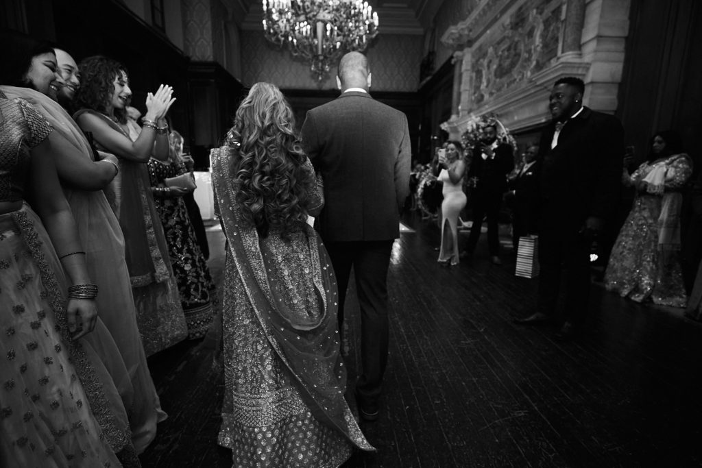 Black and white photo of the bride and groom making their entrance past applauding guests