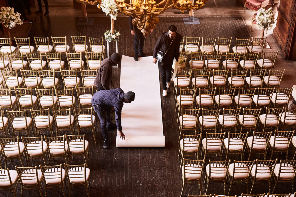 Staff laying the white aisle runner between rows of gold chairs, seen from above