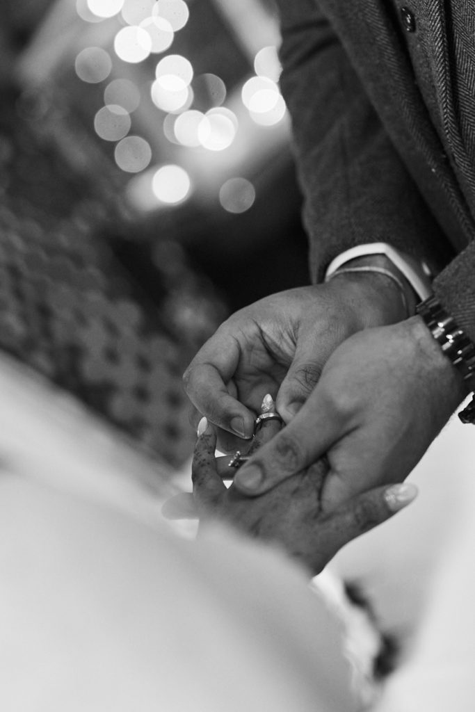 Black and white close-up of the groom placing the ring on the bride's finger