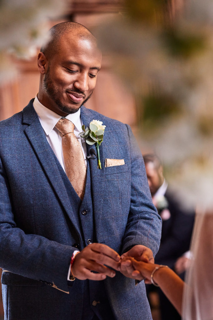 Groom smiling as he places the wedding ring on the bride's finger