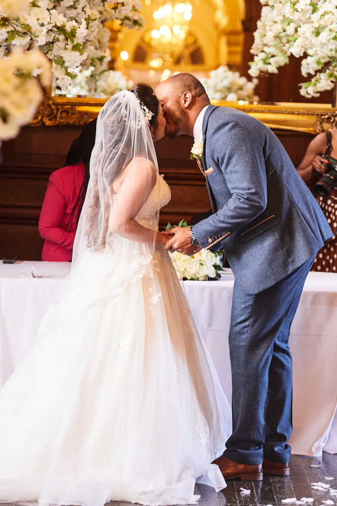 Bride and groom's first kiss under the blossom trees at Addington Palace
