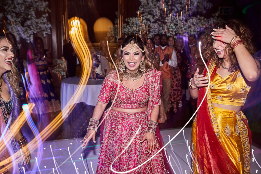 Bride in a red lehenga dancing with a bridesmaid in yellow among trails of light